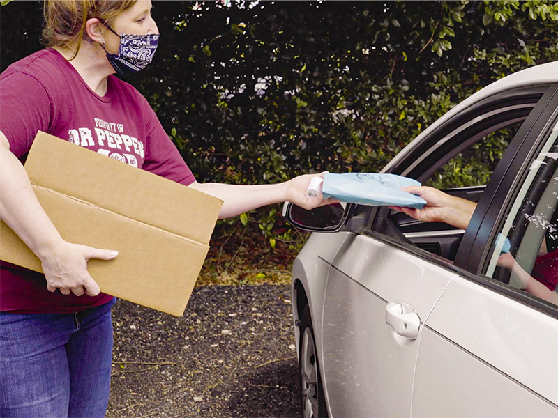 A person hands a package to a person in a car