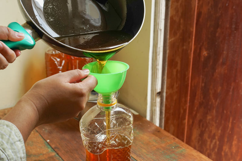 a person pours used cooking oil back into a container using a funnel